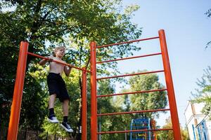 sporter pojke utför pull-ups på de horisontell bar. gata träna på en horisontell bar i de skola parkera. foto