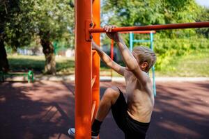 atletisk tonåring i de parkera påfrestande till klättra en turniquet. gata träna på en horisontell bar i de skola parkera. foto