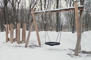 trä- lekplats tillverkad av naturlig miljövänlig material i offentlig stad parkera med snö på vinter- tid. modern säkerhet barn utomhus- Utrustning. vinter- aktiviteter. barn resten och spel på öppen luft foto