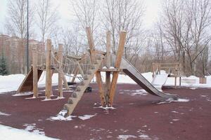 trä- lekplats tillverkad av naturlig miljövänlig material i offentlig stad parkera med snö på vinter- tid. modern säkerhet barn utomhus- Utrustning. vinter- aktiviteter. barn resten och spel på öppen luft foto