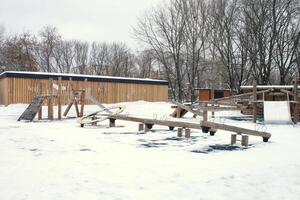 trä- lekplats tillverkad av naturlig miljövänlig material i offentlig stad parkera med snö på vinter- tid. modern säkerhet barn utomhus- Utrustning. vinter- aktiviteter. barn resten och spel på öppen luft foto