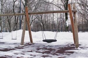 trä- lekplats tillverkad av naturlig miljövänlig material i offentlig stad parkera med snö på vinter- tid. modern säkerhet barn utomhus- Utrustning. vinter- aktiviteter. barn resten och spel på öppen luft foto