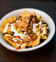 tjänande av nachos med kött, ost, vit sås och jalapenos foto