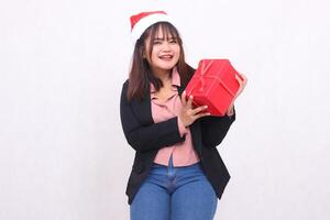 skön asiatisk flicka i kostym glad leende lutande med santa claus hatt Framställ med jul gåva låda gåva och lyft låda och kissing på vit bakgrund för befordran, reklam, banner, skylt foto
