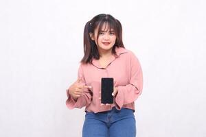 skön Lycklig asiatisk kvinna i henne 20s bär tillfällig skjorta innehav cell telefon grön skärm pekande grej från sida på vit bakgrund studio porträtt för baner annons, baner, anslagstavla foto