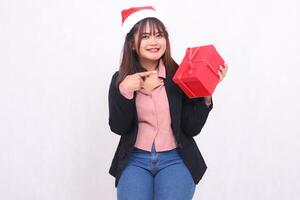 skön asiatisk flicka i kostym glad leende med santa claus hatt Framställ med jul gåva låda gåvor och lyft låda och pekande på vit bakgrund för befordran, reklam, baner, anslagstavla foto