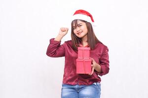 ung skön asiatisk indonesiska glad flicka bärande gåva låda i jul santa claus hatt modern röd skjorta utrusta Lycklig ser på kamera på vit bakgrund för befordran och reklam foto