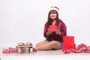 glad ung skön sydöst asiatisk flicka bärande en låda Nästa till 3 lådor av hindrar på jul bär en santa pannband och röd skjorta på en vit bakgrund för befordran och reklam foto