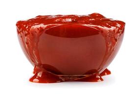 ketchup i en glas kopp isolerat på en vit bakgrund. tomat sås svämmar över över de kant av en glas skål. foto