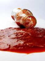 tomat sås . en glas flaska med ketchup och en pöl av ketchup spillts runt om Det. foto