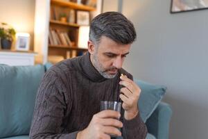 man tar medicin föreskrivs förbi hans läkare. man tar en piller och dricka en glas av vatten. hälsa, medicin, behandling begrepp foto