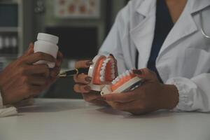 koncentrerad tandläkare Sammanträde på tabell med käke prover tand modell och arbetssätt med läsplatta och bärbar dator i dental kontor professionell dental klinik. medicinsk läkare arbetssätt foto
