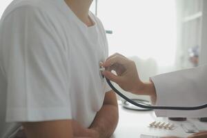 ung läkare är använder sig av en stetoskop lyssna till de hjärtslag av de patient. skott av en kvinna läkare ger en manlig patient en kolla upp upp foto