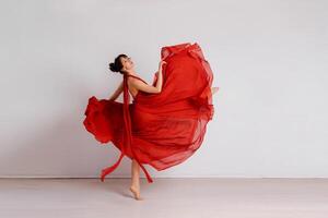 dansare i en röd flygande klänning. kvinna ballerina dans på en vit studio bakgrund foto