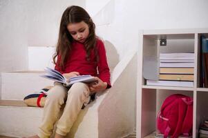 söt skola ålder barn flicka läsning en bok i mysigt Hem atmosfär, Sammanträde på steg av henne rum. de begrepp av tillbaka till skola. smart ungar, lärdom och inlärning. värld böcker dag foto