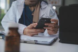 samråd uppkopplad. oigenkännlig läkare använder sig av smartphone på arbetsplats, meddelandehantering med patient, förskrivning behandling foto