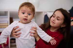 äkta porträtt av skön ungar. härlig bebis pojke 6-9 månader gammal och hans kärleksfull omtänksam syster 7 år gammal plying tillsammans på Hem foto