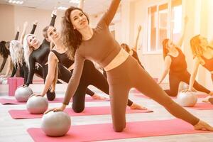 en grupp av sex atletisk kvinnor håller på med pilates eller yoga på rosa mattor i främre av en fönster i en beige loft studio interiör. lagarbete, Bra humör och friska livsstil begrepp. foto