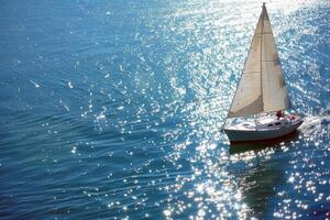 segelbåt glidande tvärs över gnistrande blå vattnen, drivs förbi mild sommar bris foto