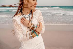 modell i boho stil i en vit lång klänning och silver- Smycken på de strand. henne hår är flätad, och där är många armband på henne vapen. foto