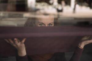 nyfiken kvinna peering genom reflekterande glas fönster i urban miljö foto