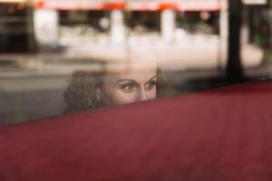 omtänksam kvinna gazing ut från Bakom en reflekterande glas fönster i en stad miljö foto