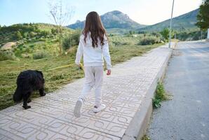 se från de tillbaka till en liten barn flicka tar henne cockerspaniel spaniel hund för en promenad på koppel i de natur mot bergen bakgrund foto