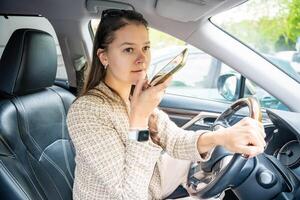 ung kvinna sändning en röst meddelande med mobil telefon inuti de bil. hög kvalitet Foto