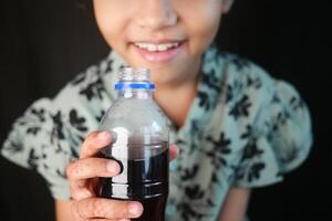 en liten flicka innehav en flaska av mjuk drycker foto
