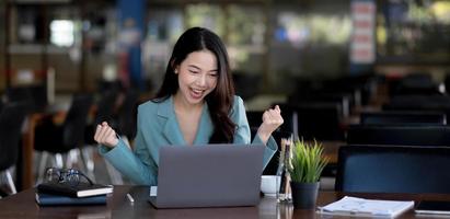 glad ung asiatisk affärskvinna sitter på sin arbetsplats på kontoret. ung kvinna som arbetar på laptop på kontoret. foto