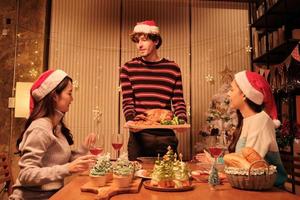 familjens speciella måltid, ung hane serverar rostad kalkon till vänner, glad med drinkar och njut av att äta, middag hemma i matsalen dekorerad för julfest och nyårsfest. foto