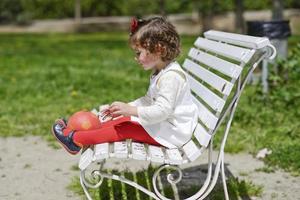 liten flicka leker med en boll som sitter på en parkbänk. foto