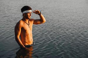 man med perfekt muskulös står i vattnet vid solnedgången foto