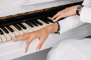 händerna på kvinnan klädd i vita kläder spelar på vitt piano foto