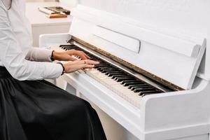 vacker kvinna klädd i vit klänning spelar på vitt piano foto