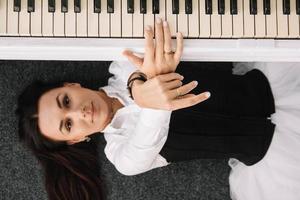 vacker kvinna klädd i en vit klänning med en svart korsett ligger på golvet nära vitt piano som spelar på tangenterna. plats för text eller reklam. utsikt från ovan
