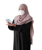 muslimsk kvinna som bär en kirurgisk mask tvättar händerna med alkoholgel på vit bakgrund. covid-19 coronavirus koncept. foto