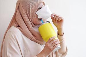 muslimsk flicka öppna en kirurgisk mask för dricksvatten på pastell bakgrund. covid-19 coronavirus koncept. foto