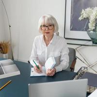 trött senior vacker grått hår kvinna i vit blus läser dokument på kontoret. arbete, seniorer, frågor, hitta en lösning, uppleva koncept