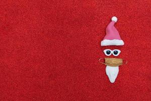 minimalistisk abstrakt jultomte i glasögon och medicinsk mask på röd bakgrund med glitter