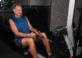 äldre mogen man tränar på en roddmaskin i gymmet foto