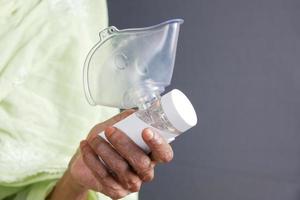 senior kvinnor hand håller en nebulisator mot ljusgrå bakgrund foto