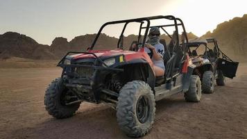 egypten, sharm el sheikh - 10 oktober 2020. aktiv kvinna kör en atv på en grusväg i öknen mot bakgrund av klippiga sandiga berg i solnedgången. foto