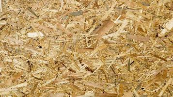 ett ark av plywood med fragment av komprimerat sågspån. konsistens av gult pressat träspån. sågspån styrelse under en press närbild. foto