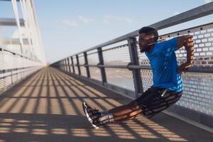 ung afrikan-amerikan man är utövar på de bro i de stad. han är håller på med omvänd armhävningar. foto