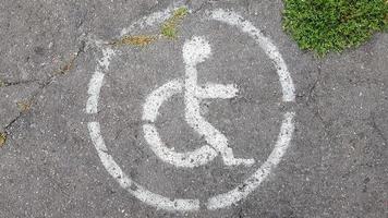 symbol för handikappparkering. handikappvik markerad med en person i rullstol skylt på grå asfalt på en stor parkeringsplats på nära håll. utsikt från ovan foto