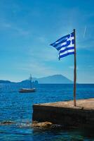 grekisk flagga i de blå himmel på pir och traditionell grekisk fiske båt i de aegean hav foto