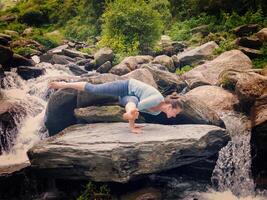 ung sportig passa kvinna håller på med yoga oudoors på tropisk vattenfall foto