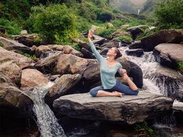 sorty passa kvinna håller på med yoga asana utomhus på tropisk vattenfall foto