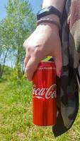 hand som håller en burk coca cola. dryckerna produceras av det amerikanska dryckesföretaget the coca-cola company. ung kvinna med coca-cola utomhus, närbild. Ukraina, Kiev - 19 augusti 2021. foto